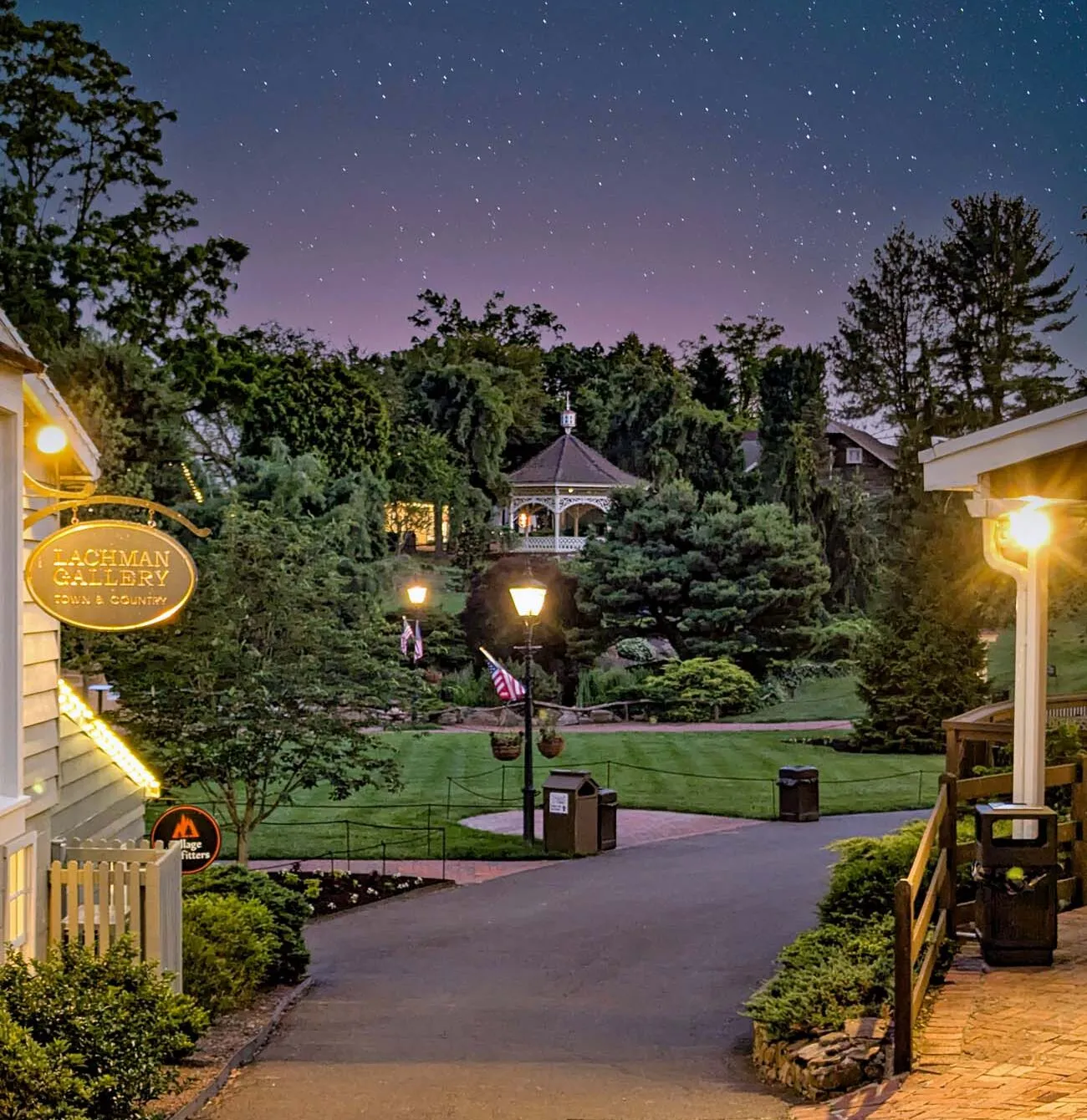 pier sixtysix flats | way of life media workforce clickbizhub magical nighttime scene of peddler's Village showing starry sky with purple and blue hues, illuminated gazebo in background, lit pathways, manicured lawns, and shop signs including Lachman Gallery, creating enchanting village atmosphere