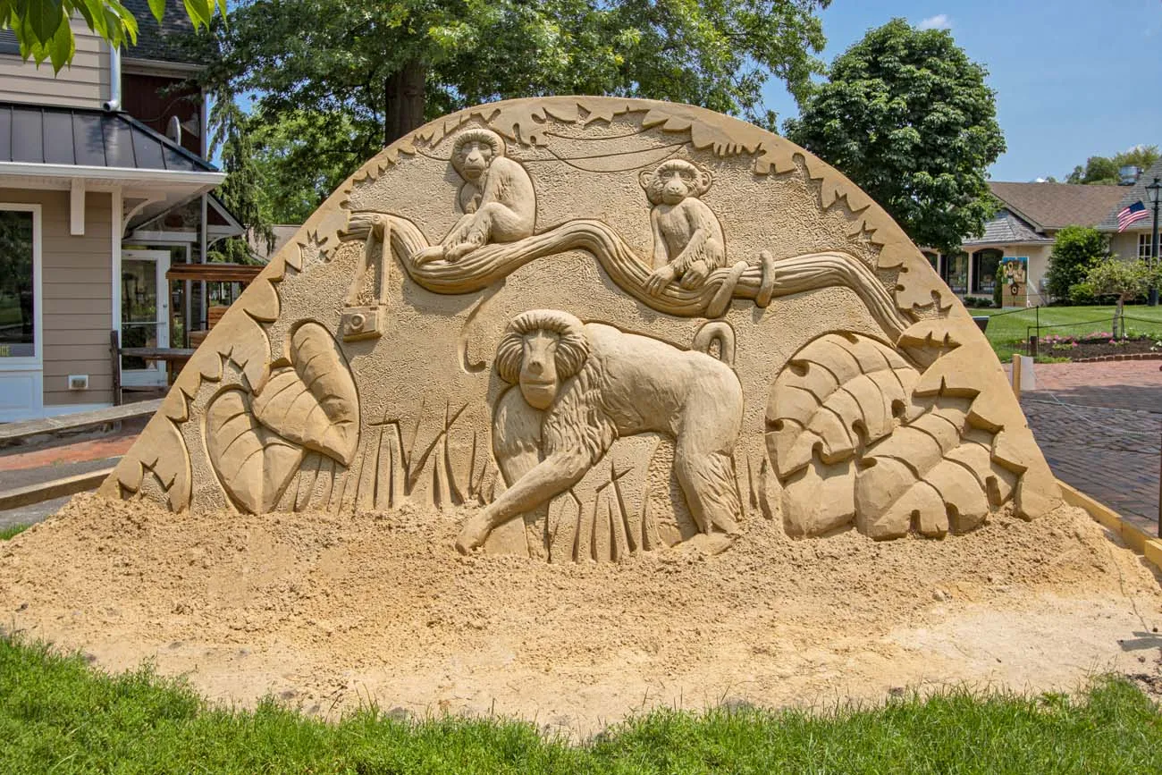 healthywomens ninth annual instructional match clickbizhub circular sand sculpture featuring carved primates sitting on tree branches at the top surrounded by decorative leaf border set on village green with colonial shops in background