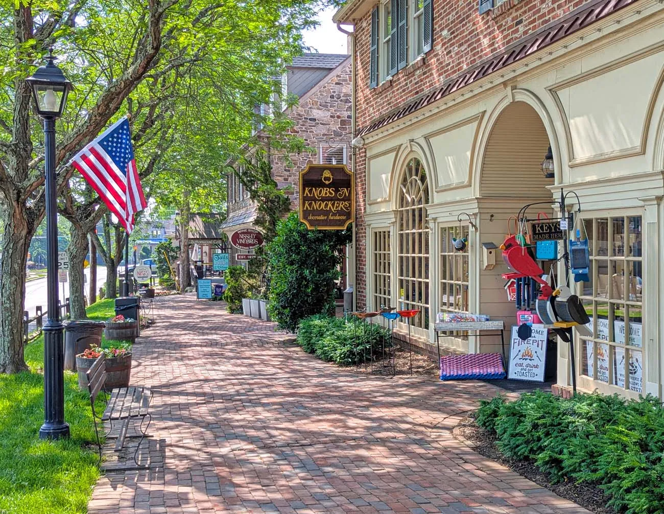 clickbizhub tree lined brick walkway through historic shopping district featuring colonial architecture with mix of brick and stone buildings american flag traditional lamp posts shop signs including