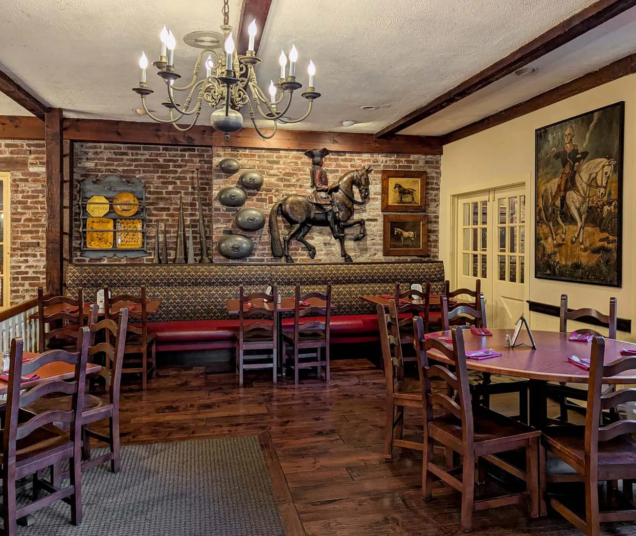 clickbizhub interior of cock 'n Bull restaurant showing colonial decor with exposed brick walls, wooden tables and chairs, brass chandelier, equestrian artwork, and traditional Pennsylvania country atmosphere